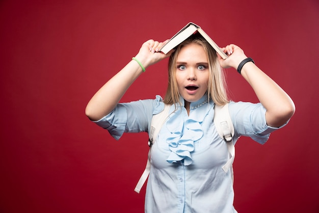 Young blonde student woman holds her book at her head and looks tired and confused