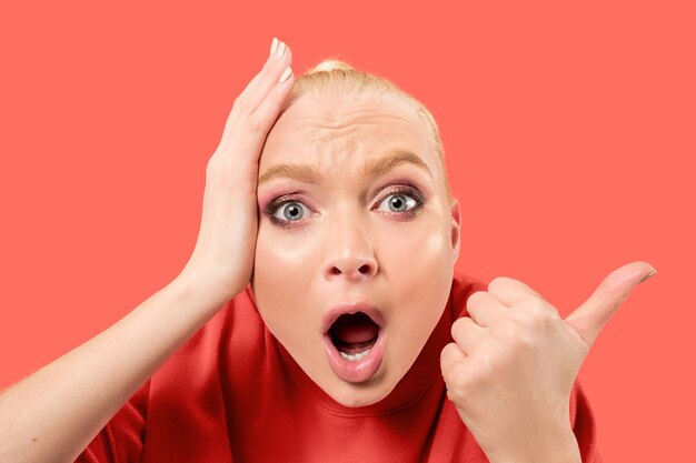 Young blonde surprised woman screaming on coral background