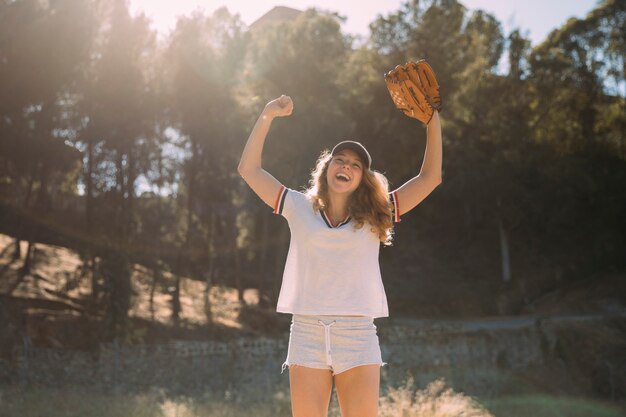 Young blonde with raised hands and baseball glove on nature background