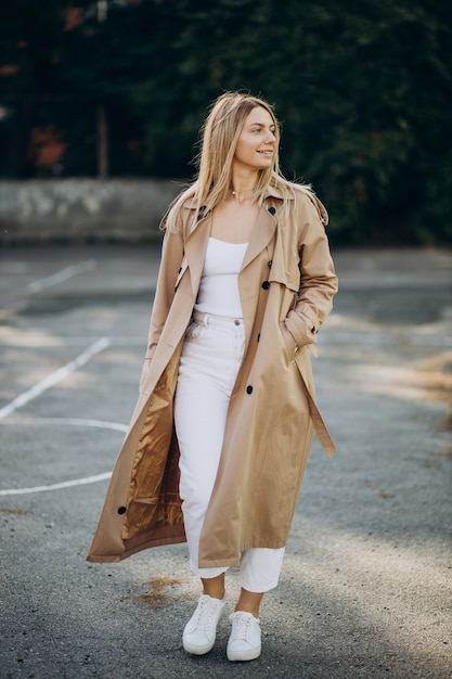 Young blonde woman in beige coat walking in the street