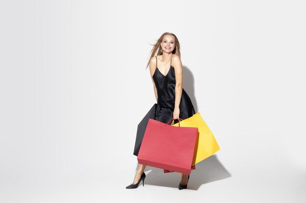 Young blonde woman in black dress shopping on white wall.