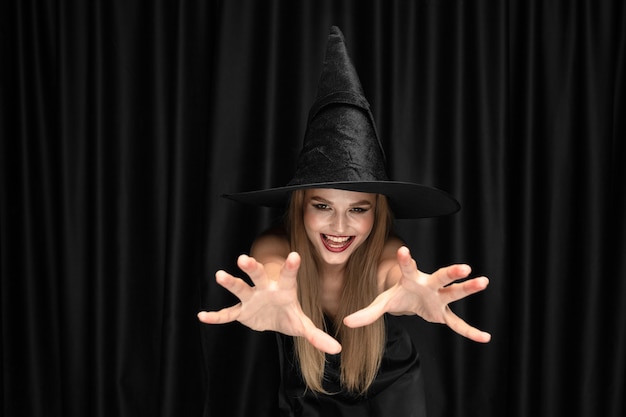 Young blonde woman in black hat and costume on black background. attractive, sensual female model. halloween, black friday, cyber monday, sales, autumn