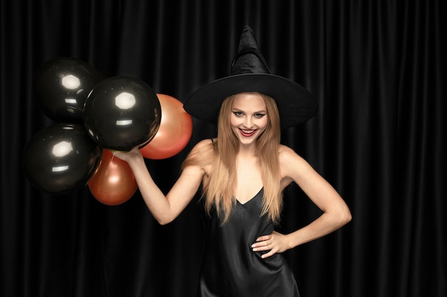 Young blonde woman in black hat and costume on black