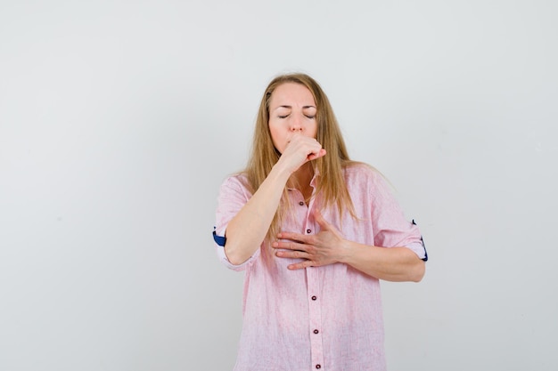 Young blonde woman in a casual pink shirt coughing