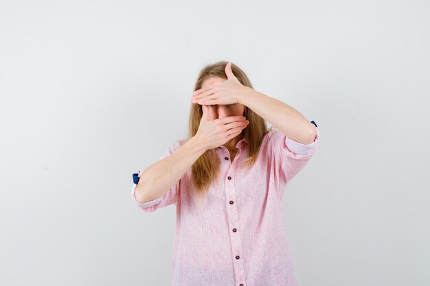 Young blonde woman in a casual pink shirt covering her face