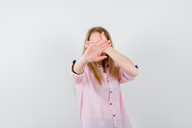 Young blonde woman in a casual pink shirt covering her face