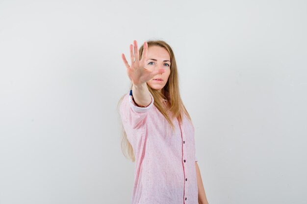 一時停止の標識を示すカジュアルなピンクのシャツを着た若いブロンドの女性