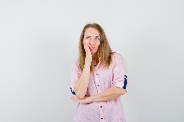 Young blonde woman in a casual pink shirt thinking