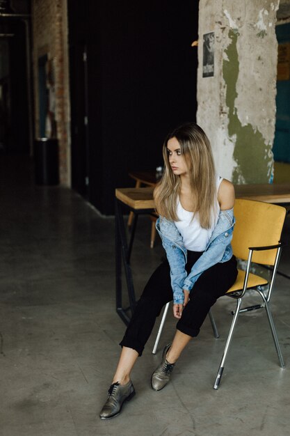 Young blonde woman dressed in casual style sits on a chair