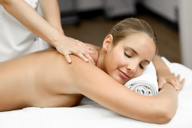 Young blonde woman having massage and smiling in the spa