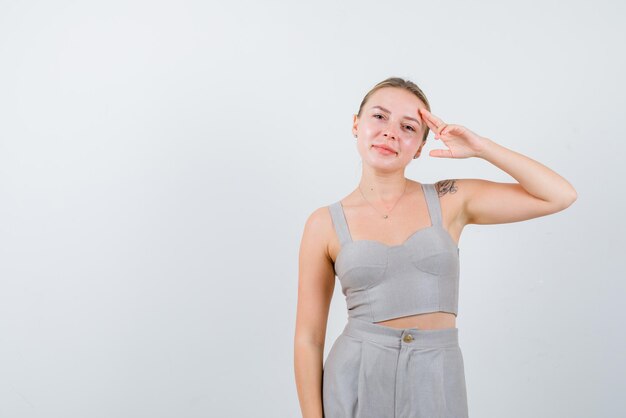 The young blonde woman is holding her forefinger on temple on white background