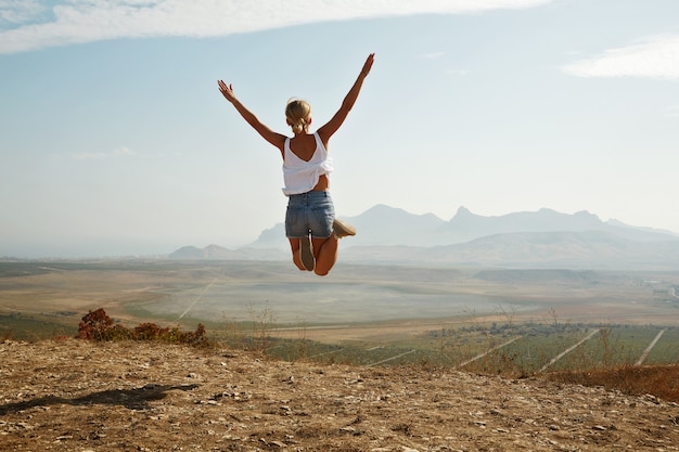Young blonde woman jumping on top of hill