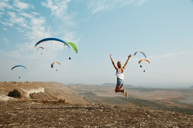 Young blonde woman jumping on top of hill