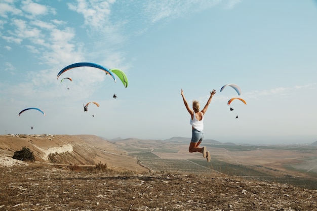 Young blonde woman jumping on top of hill