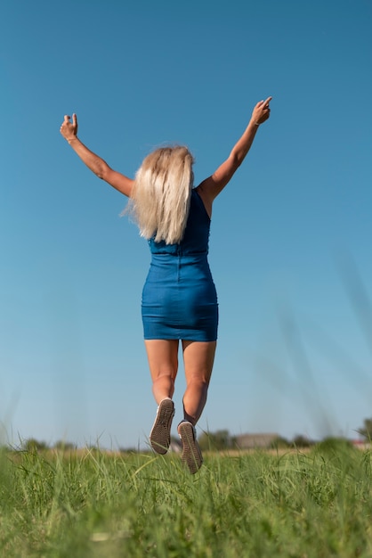 Free photo young blonde woman jumping while holding arms in the air