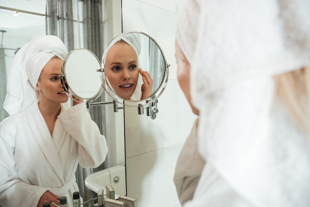 Young blonde woman looking in mirror to apply cosmetics