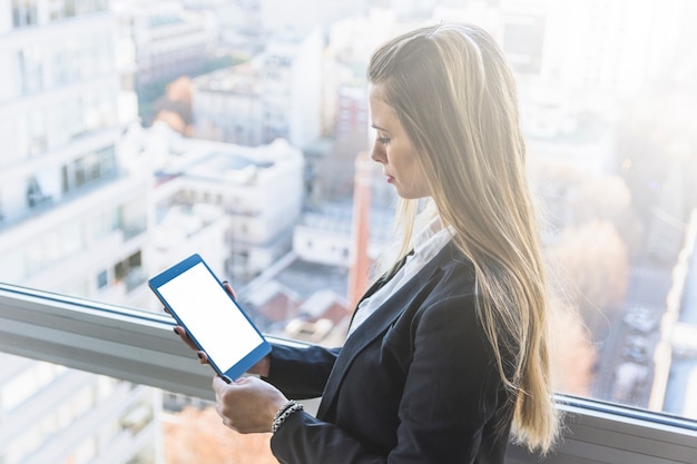 Young blonde woman looking at smartphone standing near the window