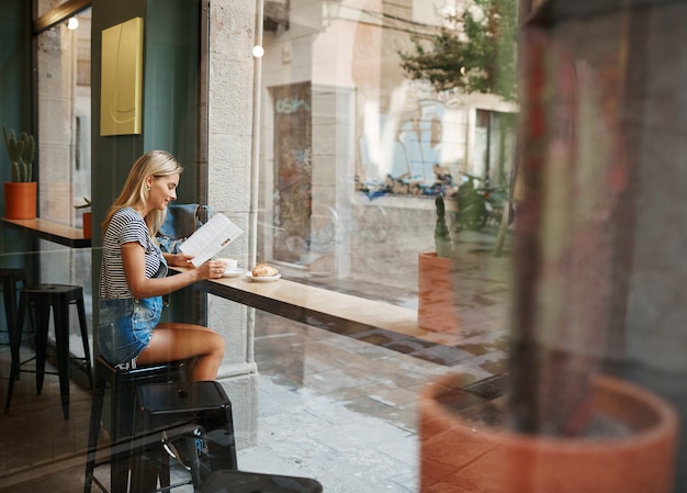 Young blonde woman sitting in cafe and reading