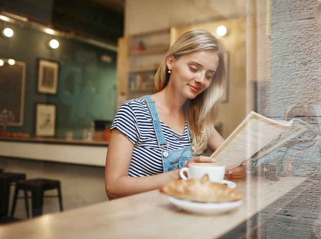 Giovane donna bionda seduta in caffè e lettura