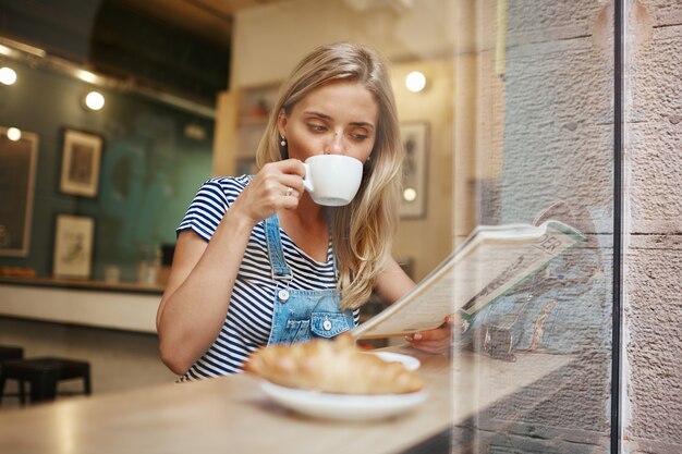 Young blonde woman sitting in cafe and reading