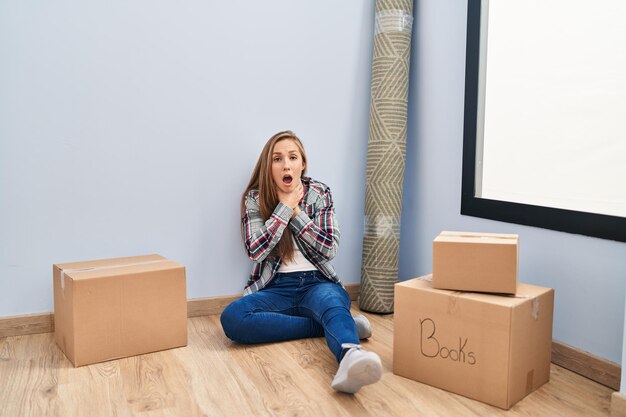 Young blonde woman sitting on the floor moving to a new home shouting and suffocate because painful strangle. health problem. asphyxiate and suicide concept.