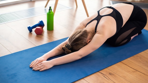 Young blonde woman in sportswear is doing yoga on a mat