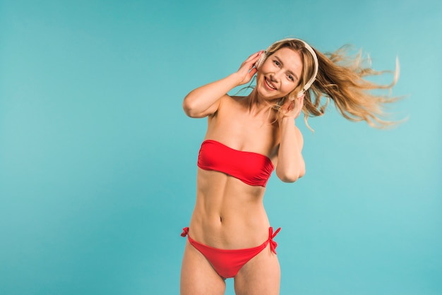 Young blonde woman in swimsuit dancing with headphones