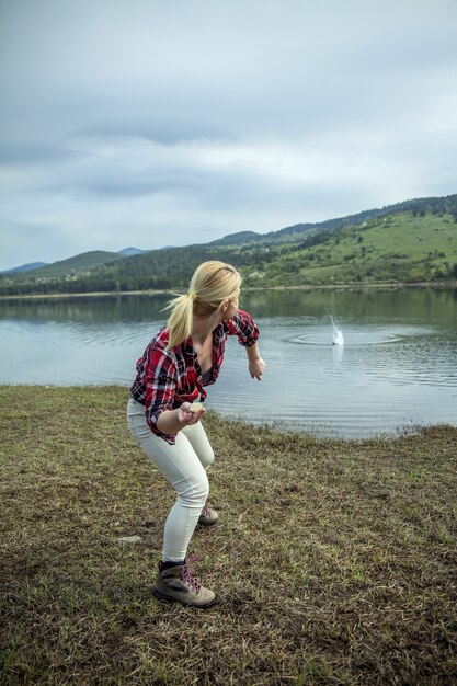 Молодая блондинка бросает камни в воду