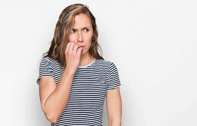 Foto gratuita giovane donna bionda che indossa abiti casual che sembra stressata e nervosa con le mani sulle unghie che mordono la bocca. problema di ansia.