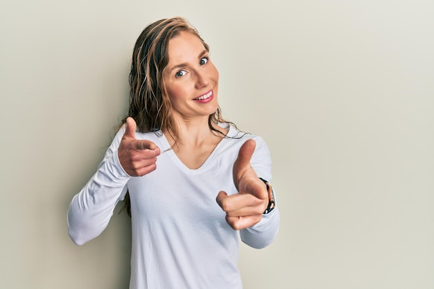 Young blonde woman wearing casual clothes pointing fingers to camera with happy and funny face good energy and vibes