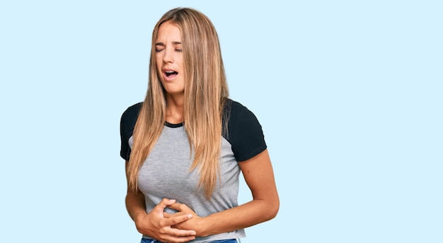 Young blonde woman wearing casual clothes with hand on stomach because nausea, painful disease feeling unwell. ache concept.