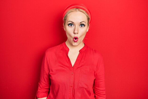 Young blonde woman wearing casual red shirt scared and amazed with open mouth for surprise disbelief face