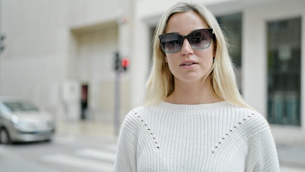 Молодая блондинка в солнцезащитных очках с серьезным выражением лица на улице