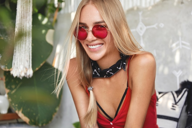 young blonde woman with a red stylish sunglasses, poses indoor