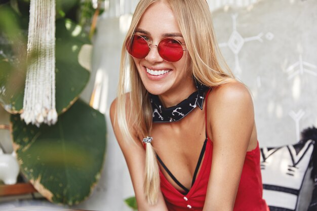 young blonde woman with a red stylish sunglasses, poses indoor