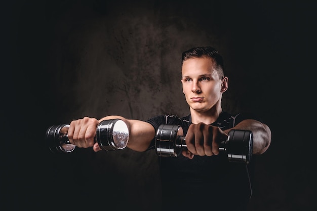 Free photo a young bodybuilder wearing sportswear doing exercise with dumbbells on a dark background.