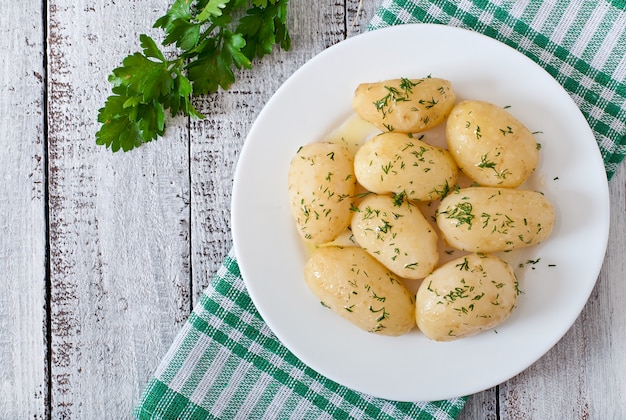 Молодой отварной картофель с маслом и укропом на белой тарелке