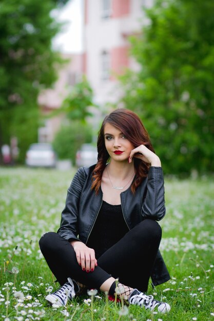 Young Bosnian woman sitting on the grass with dandelions around her in the park