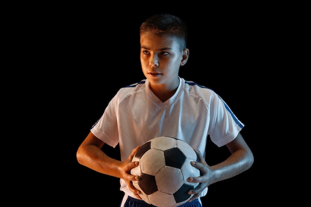 Мальчик в футболе или футболисте в спортивной одежде делает финт или удар мячом по воротам на темном фоне.