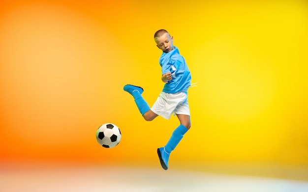 Young boy as a soccer or football player in sportwear practicing on gradient wall
