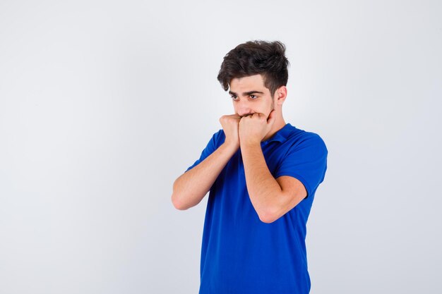 Young boy in blue t-shirt biting fists and looking serious , front view.