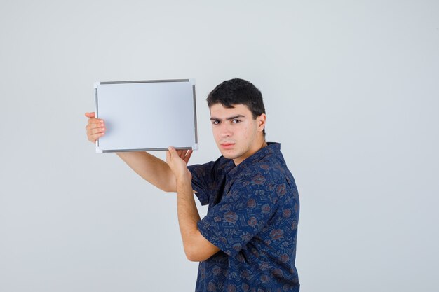 Young boy in floral shirt holding whiteboard and looking serious