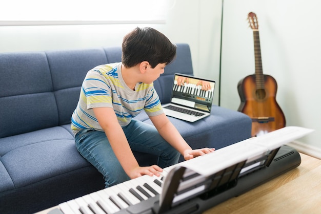 Young boy following the instructions of the music teacher and learning to play the piano. Caucasian kid taking art lessons on an online video call