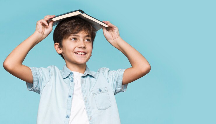 मुफ़्त फोटो young boy holding book on his head