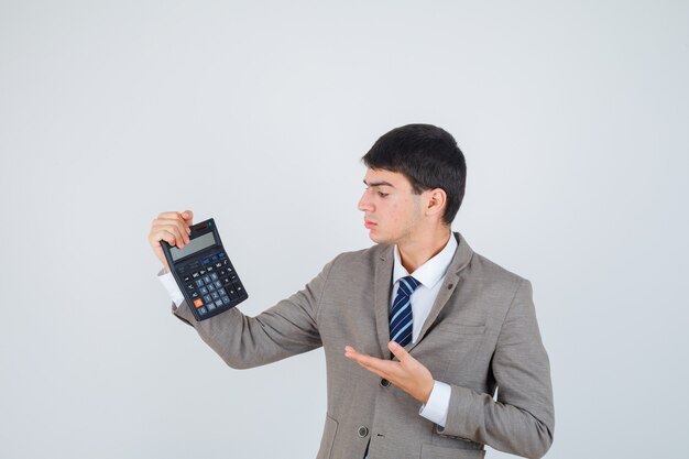 Young boy holding calculator, stretching hand as presenting it in formal suit