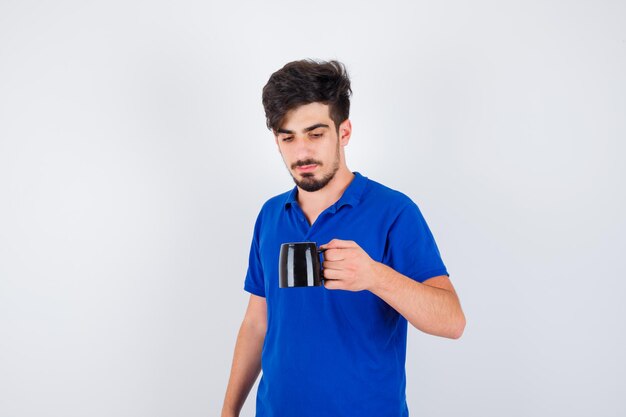 Young boy holding cup in blue t-shirt and looking serious , front view.