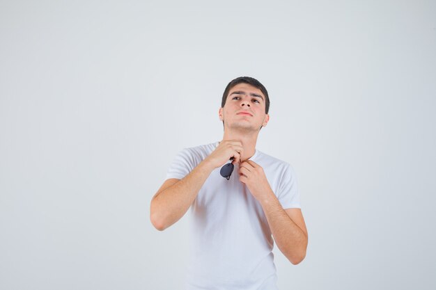 Young boy holding glasses, looking upwad in t-shirt and looking self-confident. front view.