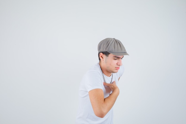 Бесплатное фото Молодой мальчик, держащий руку на груди в футболке, шляпе и задумчивый. передний план.