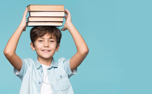 Free photo young boy holding stack of books on head