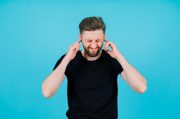 Young boy is holding forefingers in ears on blue background